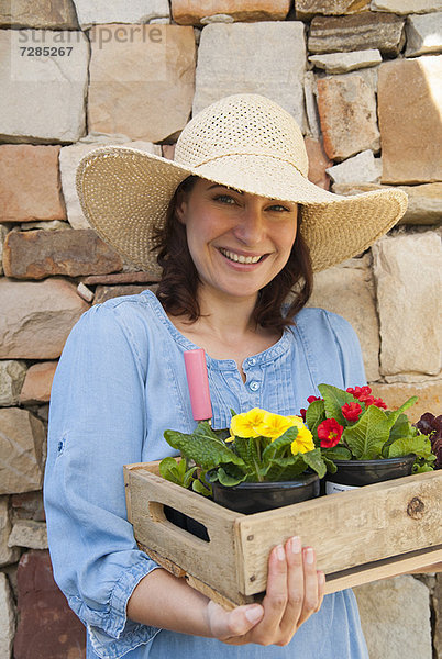 Frau  die eine Holzkiste mit Blumen trägt.