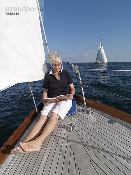 Ältere Frau beim Lesen auf dem Segelboot