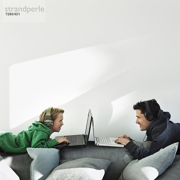 Vater und Sohn mit Laptops auf dem Sofa