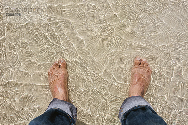 Mans Füße im klaren Wasser am Strand