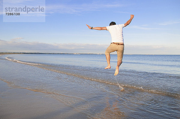 Mann springt vor Freude in den Wellen am Strand