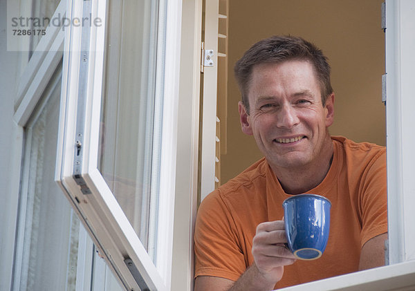 Mann mit aus dem Fenster lehnendem Kaffee