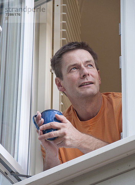 Mann mit aus dem Fenster lehnendem Kaffee