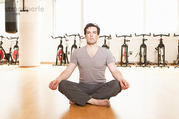Mann meditiert auf Matte im Fitnessstudio