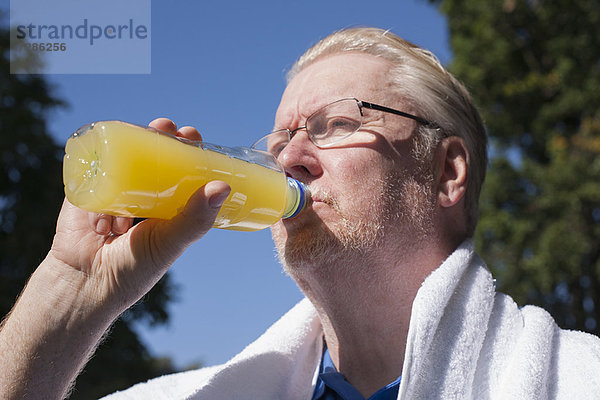 Älterer Mann trinkt Orangensaft im Freien