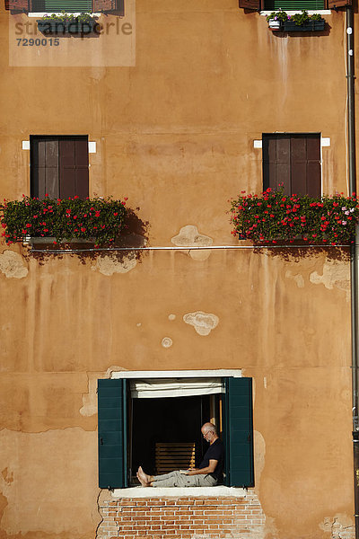 Mann sitzt lesend im Fenster  Venedig  Italien