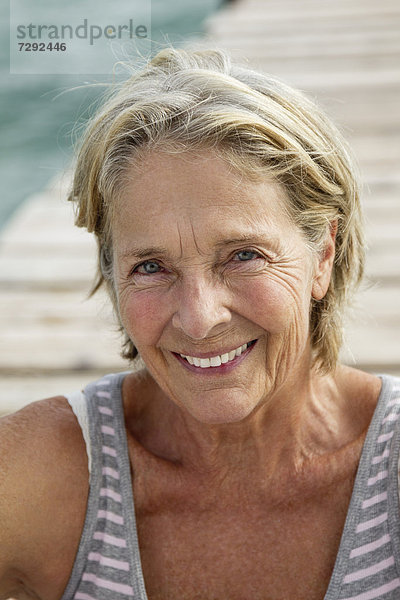 Spain  Senior woman sitting on jetty at the sea  smiling  portrait