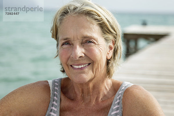Spain  Senior woman sitting on jetty at the sea  smiling  portrait