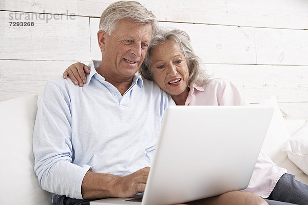 Spain  Senior couple checking emails on laptop  smiling