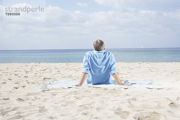 Spanien  Senior am Strand sitzend