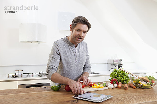 Mann  der Essen zubereitet  während er nach einer digitalen Tablette sucht