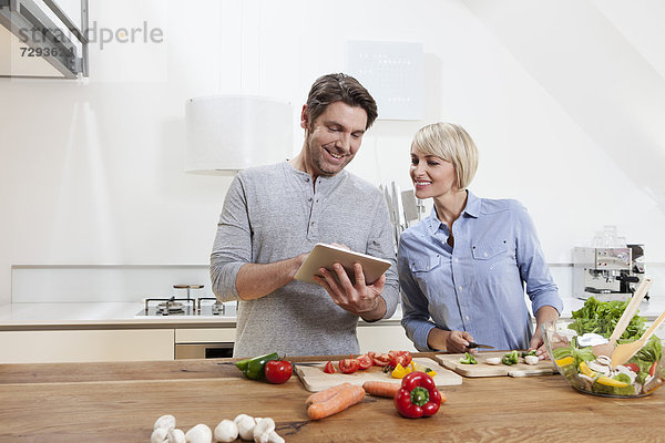 Deutschland  Bayern  München  Reife Paare beim Zubereiten von Speisen mit Blick auf digitale Tabletten