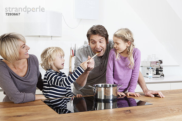 Familie bereitet Essen in der Küche zu  während der Junge den Vater füttert.