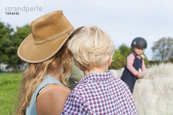 Germany  Munich  Mother and children at children's camp  daughter riding horse in background