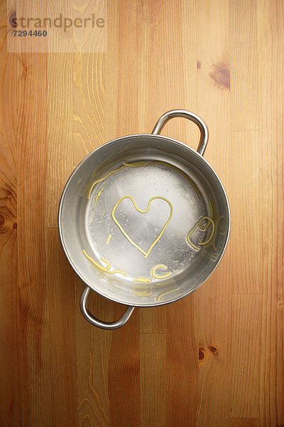 Herzförmige Spaghetti im Kochtopf auf Holztisch