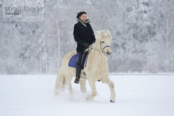 Junge Frau reitet auf Pferd im Schnee