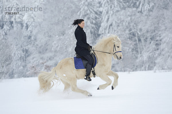 Junge Frau reitet auf Pferd im Schnee