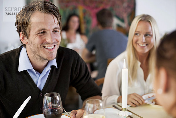 Glücklicher junger Mann mit Freunden am Restauranttisch