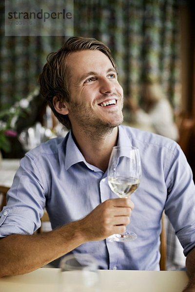 Fröhlicher junger Mann mit Weinglas am Restauranttisch und Blick nach oben