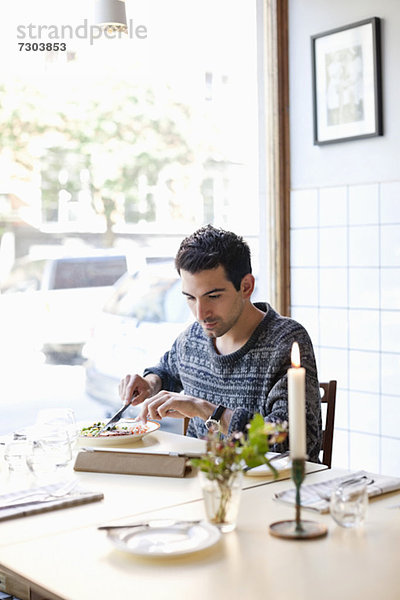 Junger Mann am Restauranttisch beim Essen mit digitalen Tabletten