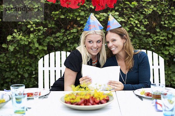 Fröhliche weibliche Freunde mit einer Karte  die während der Krebsparty auf den Esstisch schaut.