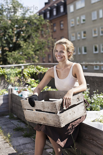 Glückliche junge Frau mit Holzkiste sitzend im Stadtgarten