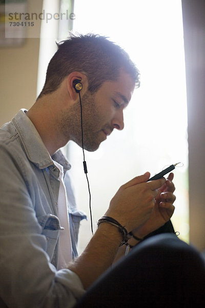 Seitenansicht des jungen Mannes beim Musikhören über das Handy