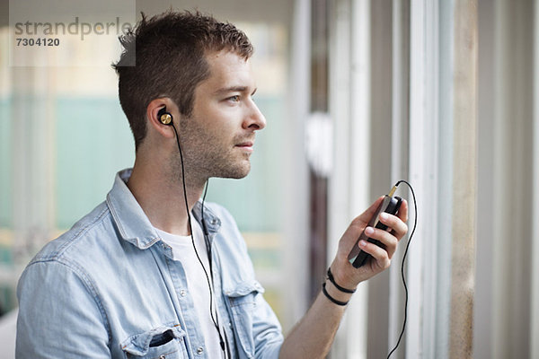 Seitenansicht des nachdenklichen jungen Mannes beim Musikhören per Handy