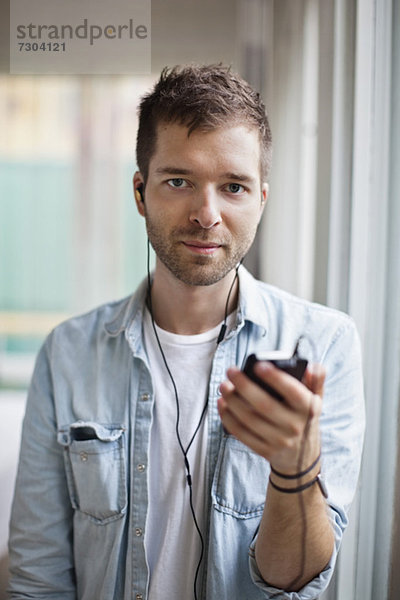 Porträt eines jungen Mannes  der Musik über das Handy hört.