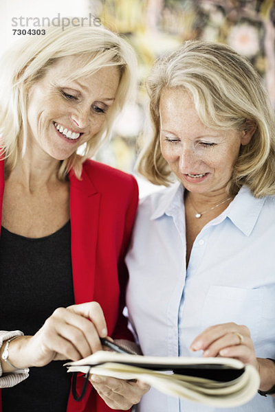 Fröhliche Geschäftsfrauen diskutieren Notizen im Büro