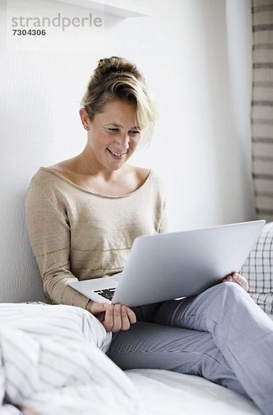 Glückliche Frau mit Laptop im Bett zu Hause