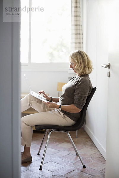 Senior Geschäftsfrau mit Laptop im Sitzen auf dem Stuhl zu Hause
