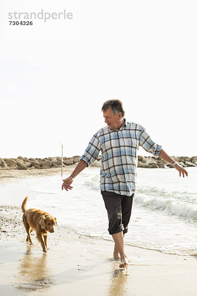 Älterer Mann  der mit Hund am Strand spazieren geht