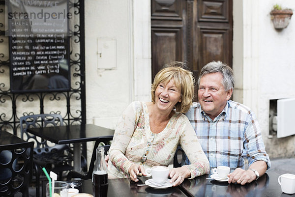 Ein glückliches Paar schaut weg  während es am Tisch Kaffee trinkt.
