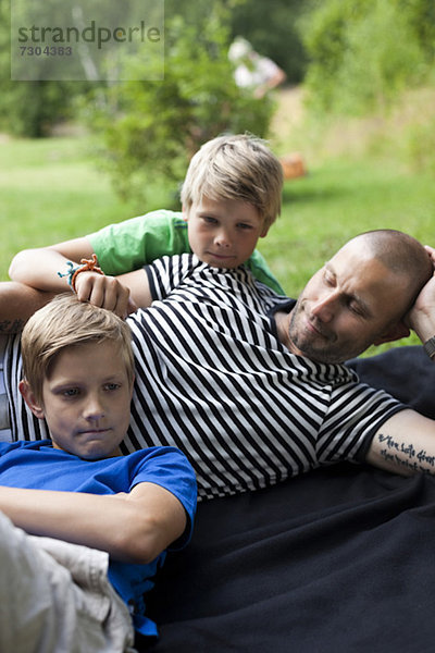 Erwachsener Mann mit Söhnen  die auf Gras im Park liegen