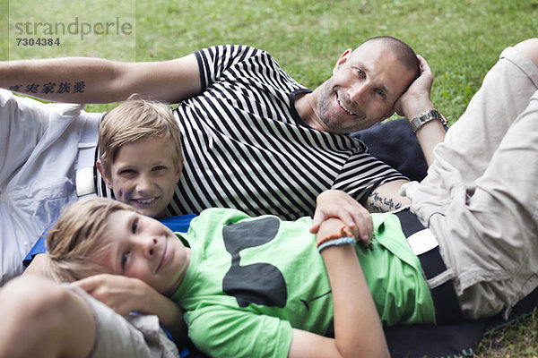Porträt eines glücklichen reifen Mannes mit Söhnen auf Gras im Park