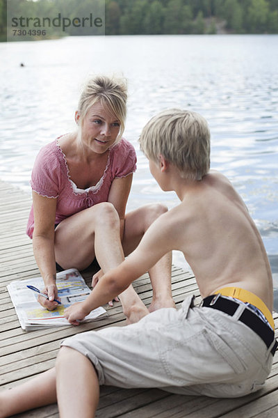 Reife Frau  die auf Zeitungen schreibt  während sie mit ihrem Sohn auf dem Pier redet