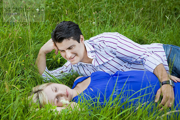 Mann liegt mit seiner schwangeren Frau im Gras und sieht sie zärtlich an