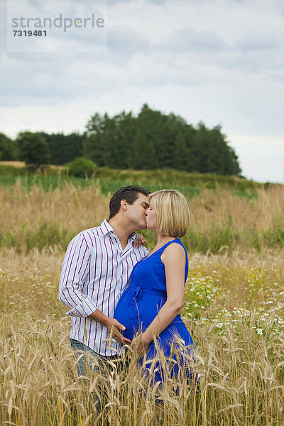 Mann und schwangere Frau küssen sich in einem Feld