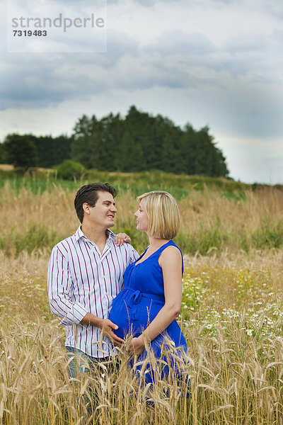 Mann und schwangere Frau umarmen sich in einem Feld