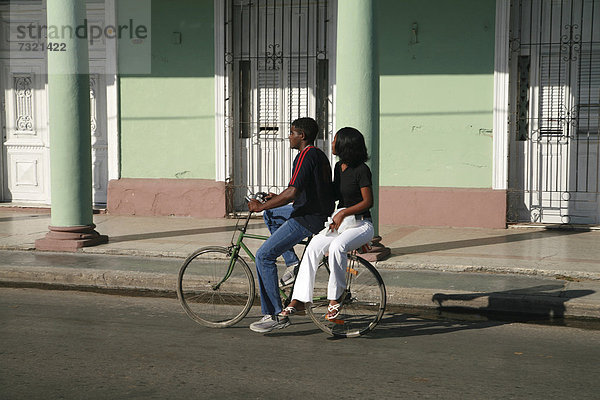 Ein Fahradfaher mit Beifahrerin auf dem Gepäckträger in Cienfuegos  Kuba  Amerika