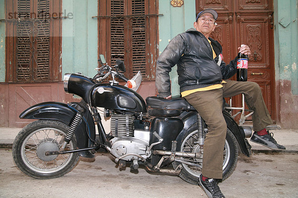 Ein älterer Mann auf seinem Motorrad mit einer Flasche der heimischen Cola (tu cola) in Havanna  Kuba  Amerika