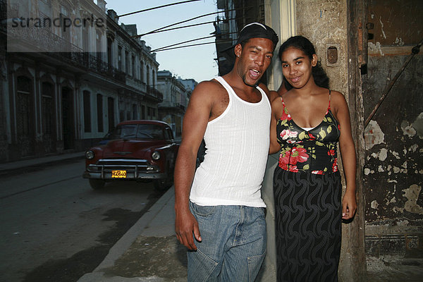 Ein junger Mann mit seiner Frau und im Hintergrund ein Oldtimer in den Straßen von Havanna  Kuba  Amerika