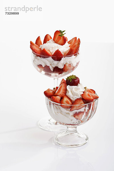Zwei Glasbecher mit Erdbeeren und Sahne