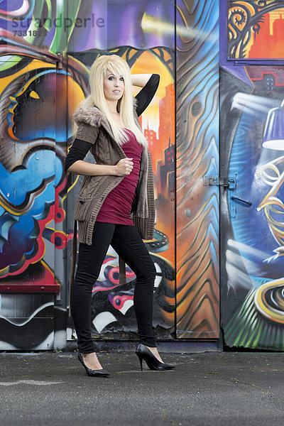 Junge Frau mit langen blonden Haaren posiert vor Graffitiwand