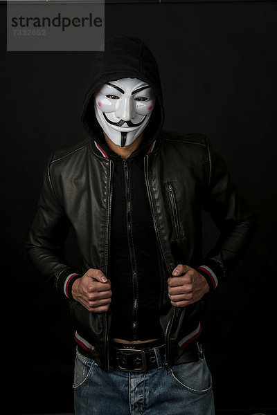Junger Mann mit Anonymus-Maske  Kapuze und schwarzer Lederjacke
