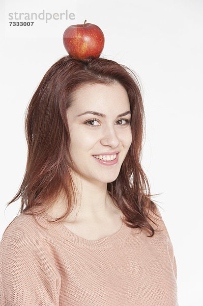 Lächelnde junge Frau mit einem Apfel auf ihrem Kopf