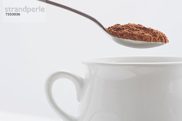 Weiße Tasse und Löffel mit Kakaoppulver
