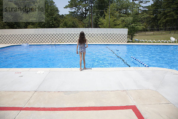 Ein Mädchen steht am Rande eines Swimmingpools.