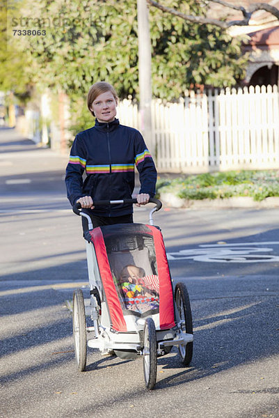 Eine Frau  die auf der Straße geht und einen Kinderwagen schiebt.